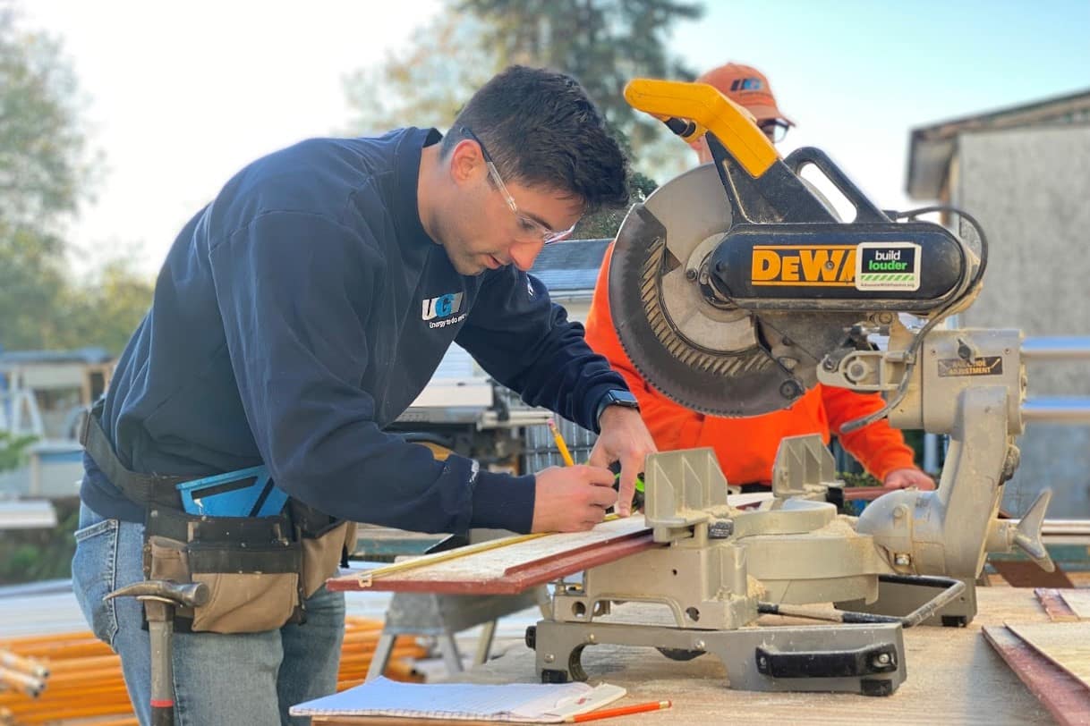 UGI employee with safety goggles and toolbelt working cutting wood with a saw